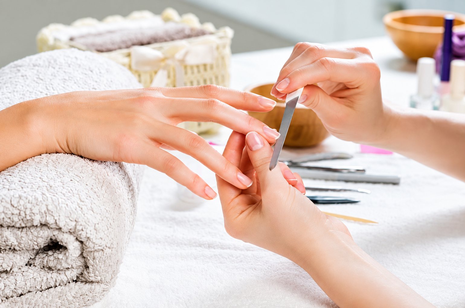 Une manucure limant les ongles d'une cliente dont la main repose sur une serviette blanche, avec des outils posés sur la table.